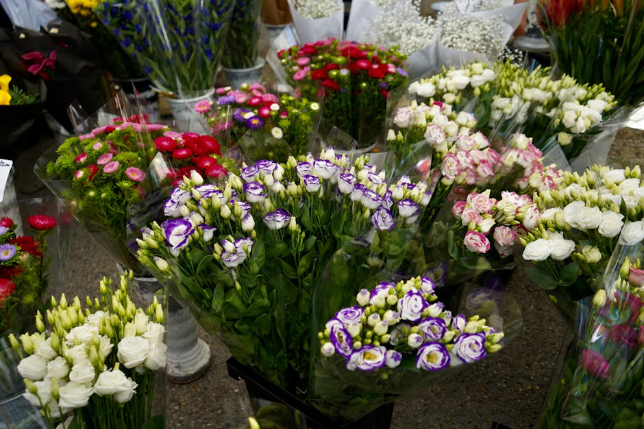 A vibrant display of fresh flower bouquets arranged in clear plastic wrapping, featuring a variety of blooms including purple and white eustoma roses, pink and white spray roses, bright red carnations
