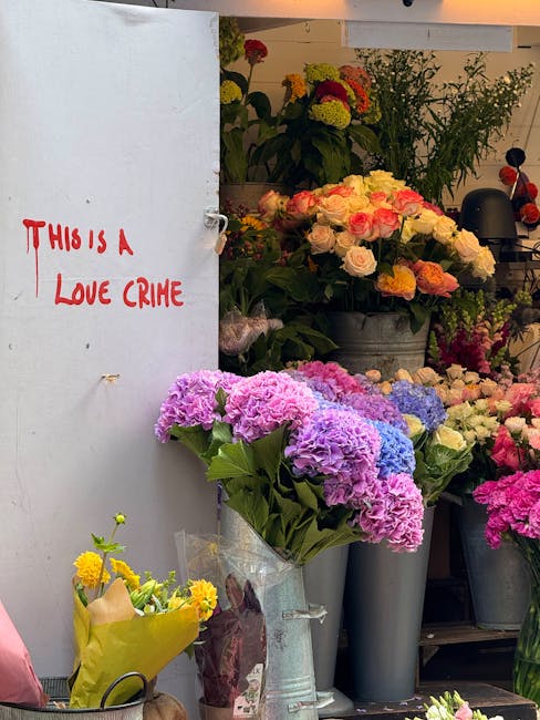 A display of fresh floral arrangements at a flower shop, featuring large hydrangea bouquets in shades of purple, pink, and blue wrapped in clear plastic, placed in a tall, grey vase on a shelf. Behind
